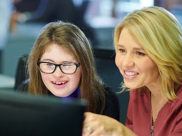 A person with disability working with someone else on a computer. 