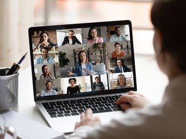 A person on a laptop in a video call with many people.