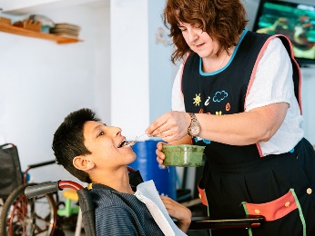 A woman feeding a boy in a wheelchair.