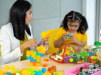 A woman and a young girl playing with building blocks together. 