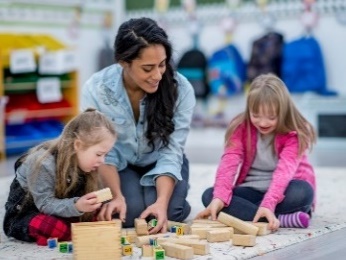 A woman and two young girls playing with building blocks together. 