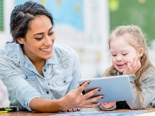 A woman helping a young girl read on an iPad. 